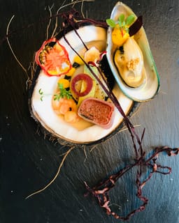 Halbe Kokosnuss mit kleinen Häppchen und einer Muschel, auf Schiefer angerichtet