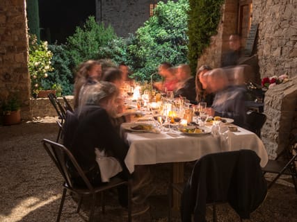 Gäste an einer langen, gedeckten Tafel im Freien, abends bei Kerzenlicht