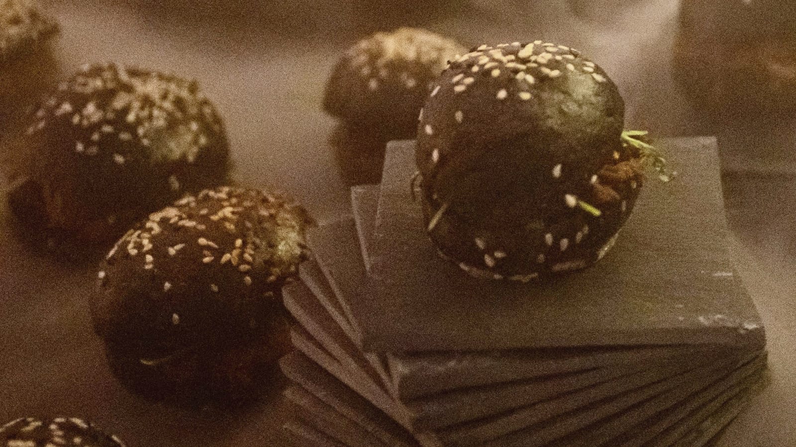 Nahaufnahme: Mini-Burger mit schwarzem Brot und Sesam auf einem Stapel Schieferplatten
