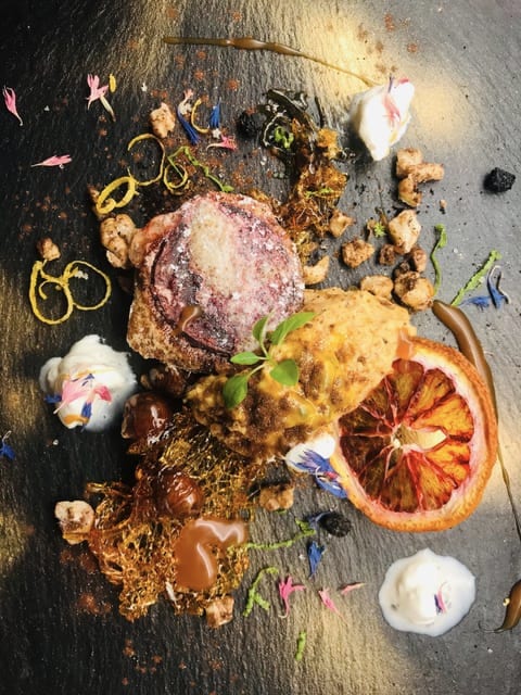 Angerichtetes Dessert auf Schiefer mit getrockneter Blutorange, Crèmetupfen und Blüten