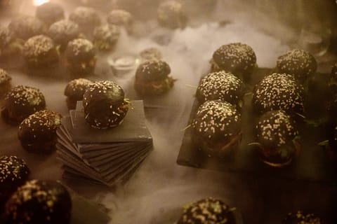 Viele Mini-Burger mit schwarzem Brot und Sesam auf Schieferplatten, dazwischen Nebel