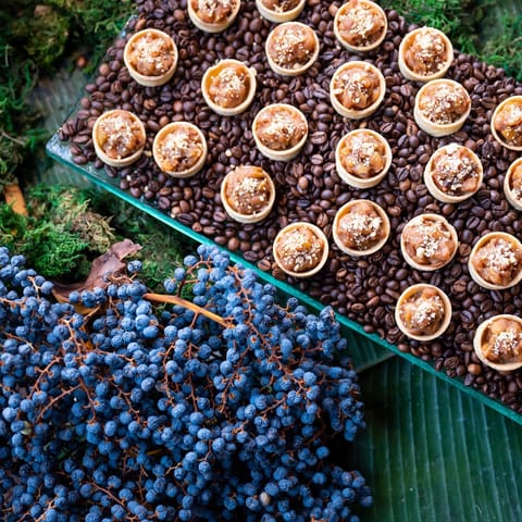 Mini-Tartelettes mit Crème auf Kaffeebohnen, davor blaue Beerenzweige