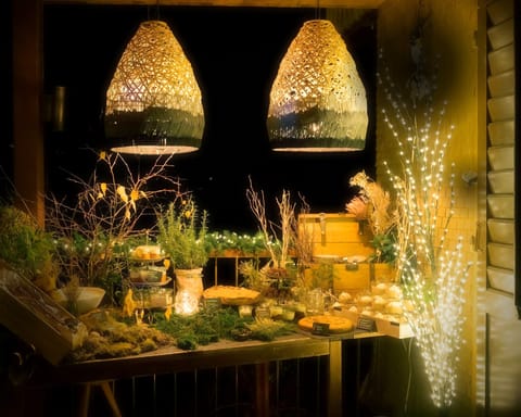 Waldbuffet bei Nacht auf einer Terrasse: Moos, Zweige und Holzkisten mit Speisen unter zwei geflochtenen Hängelampen, daneben Lichterketten