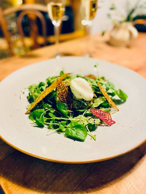 Salat mit Blättern, Kräutern und einer weissen Nocke auf einem hellen Teller