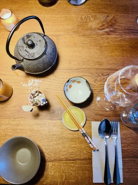 Gedeckter Holztisch von oben: gusseiserne Teekanne, kleine Schalen, Stäbchen und Besteck