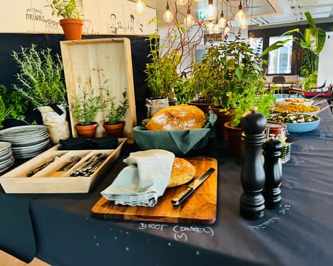 Buffet mit Kräutertöpfen, Brot auf dem Holzbrett, Pfeffermühlen und Besteck in einer Holzkiste