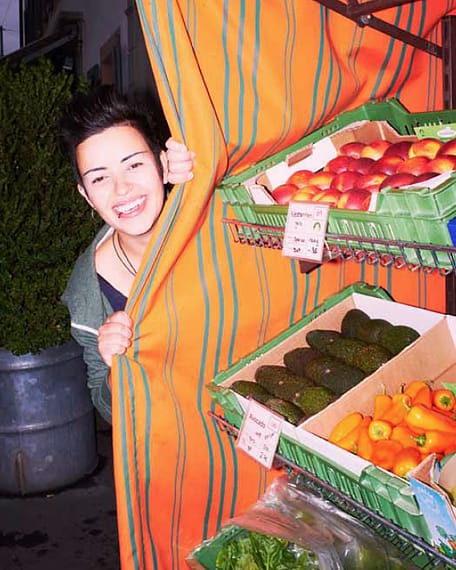 Lia Santos lacht hinter dem Vorhang eines Marktstands hervor